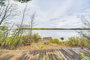 A wooden deck overlooking a calm lake with trees and a distant shoreline. - Private Peninsula! Modern-rustic Fall Lake Cabin (Ely)