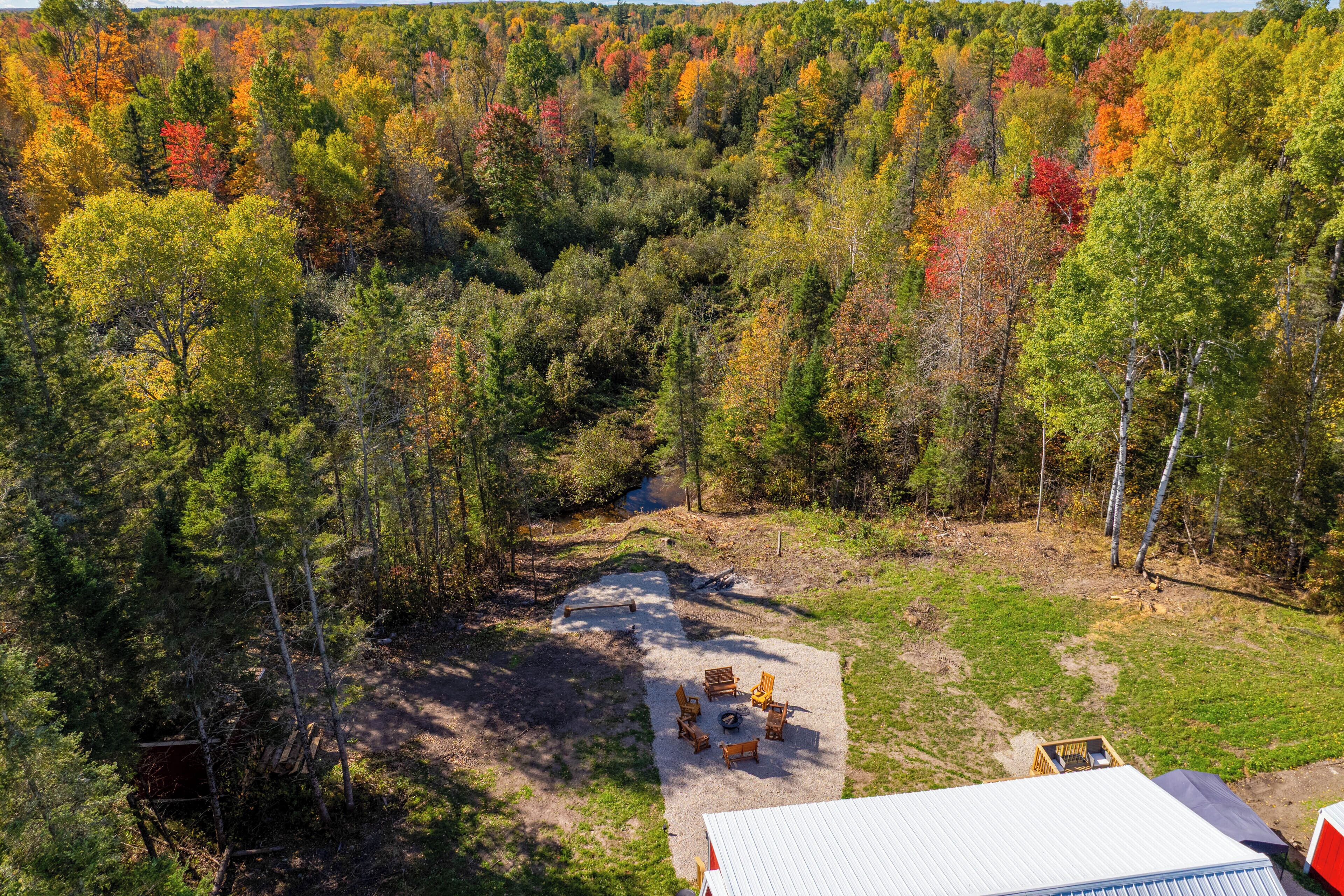 An aerial view of a forested area with a clearing containing outdoor seating and a building with a white roof.