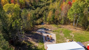 An aerial view of a forested area with a clearing containing outdoor seating and a building with a white roof.