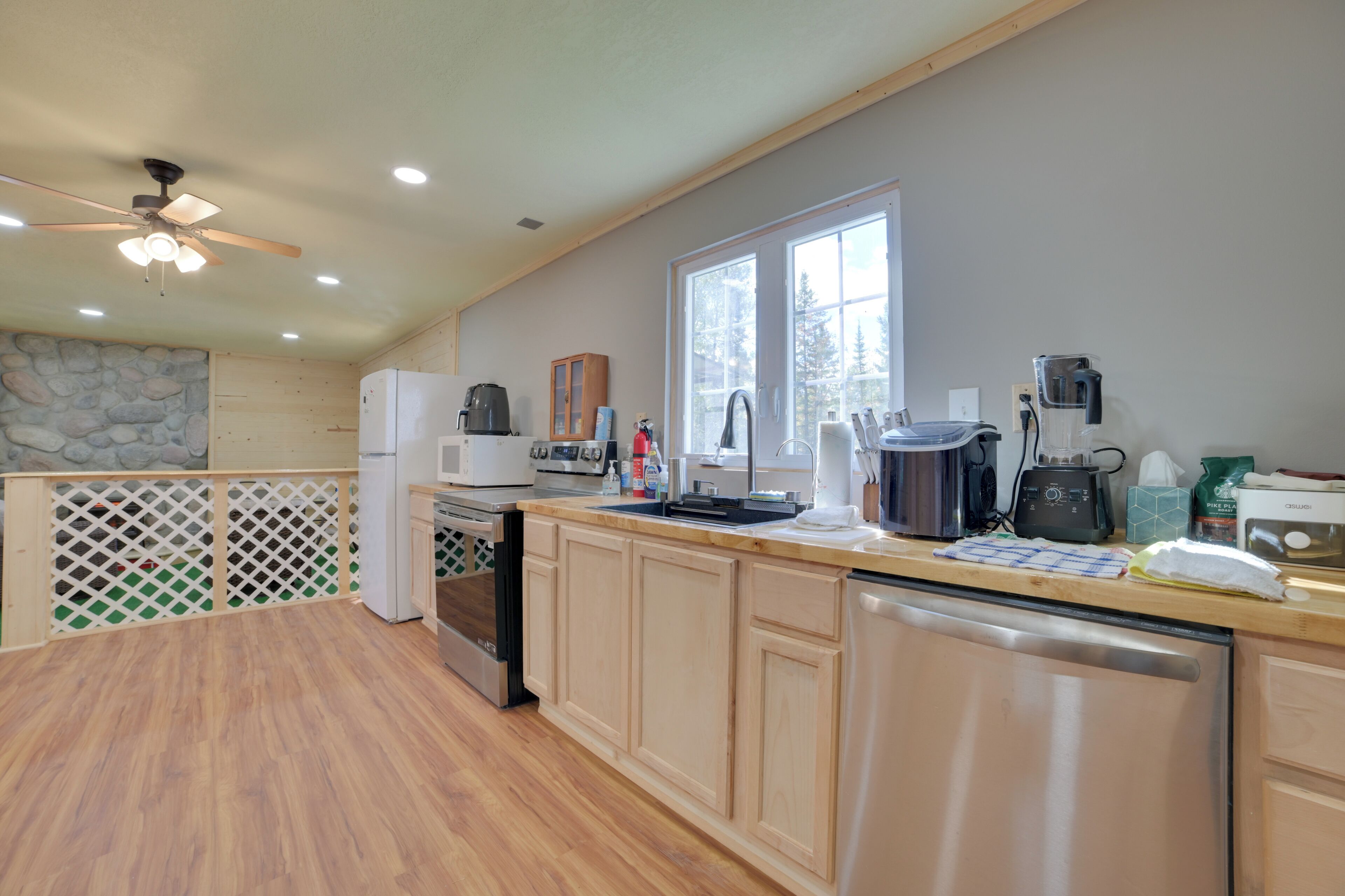 A kitchen with wooden cabinets, a refrigerator, a stove, and a dishwasher. There is a window providing natural light and a view of trees.