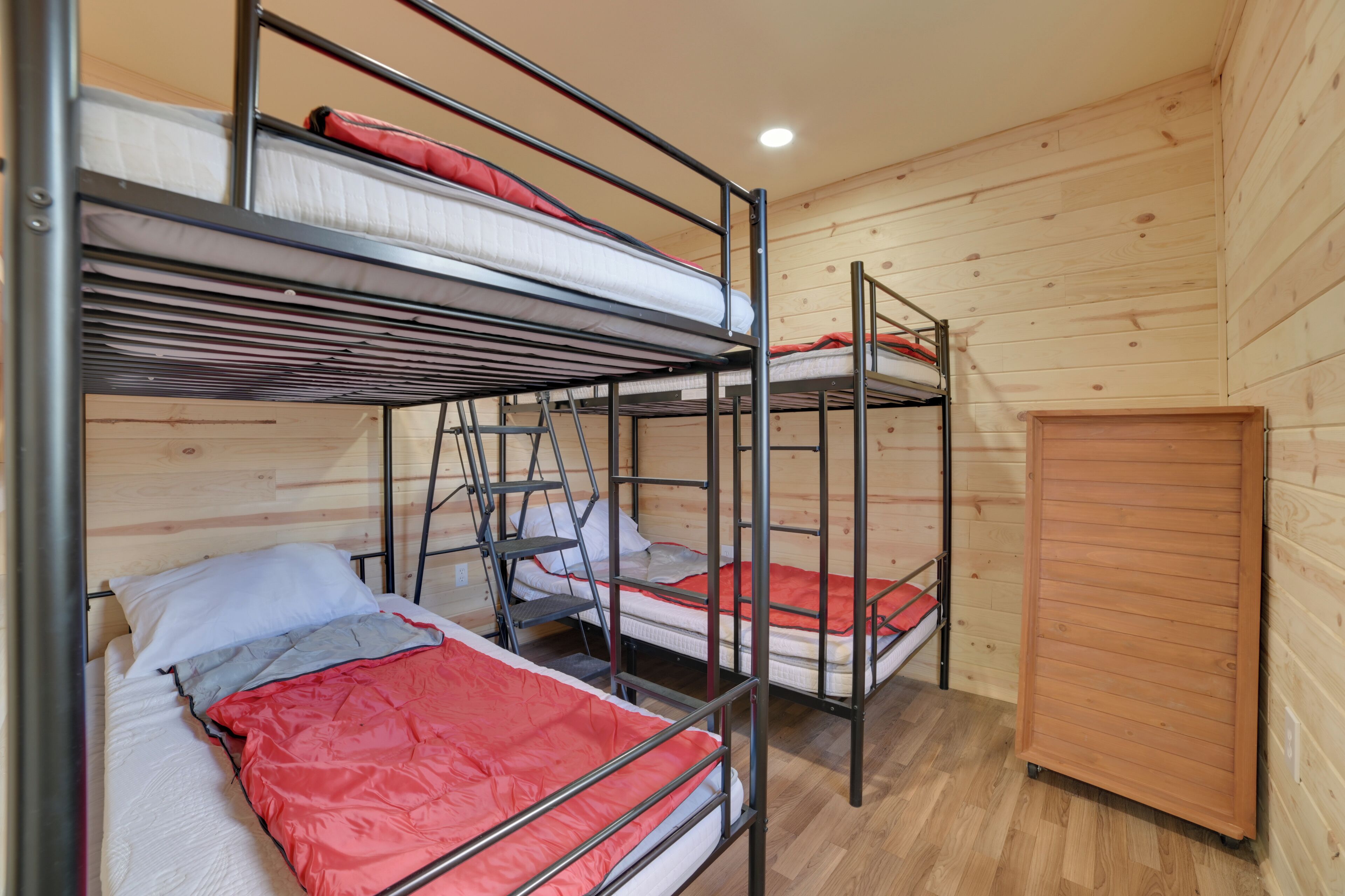 A bunk room with three metal bunk beds, wooden walls, and a small wooden cabinet.