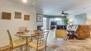 A spacious living room with a glass dining table, comfortable seating, a fireplace, and a large window. - Waterfront Balcony! Condo on Lake of the Ozarks (Lake Ozark)