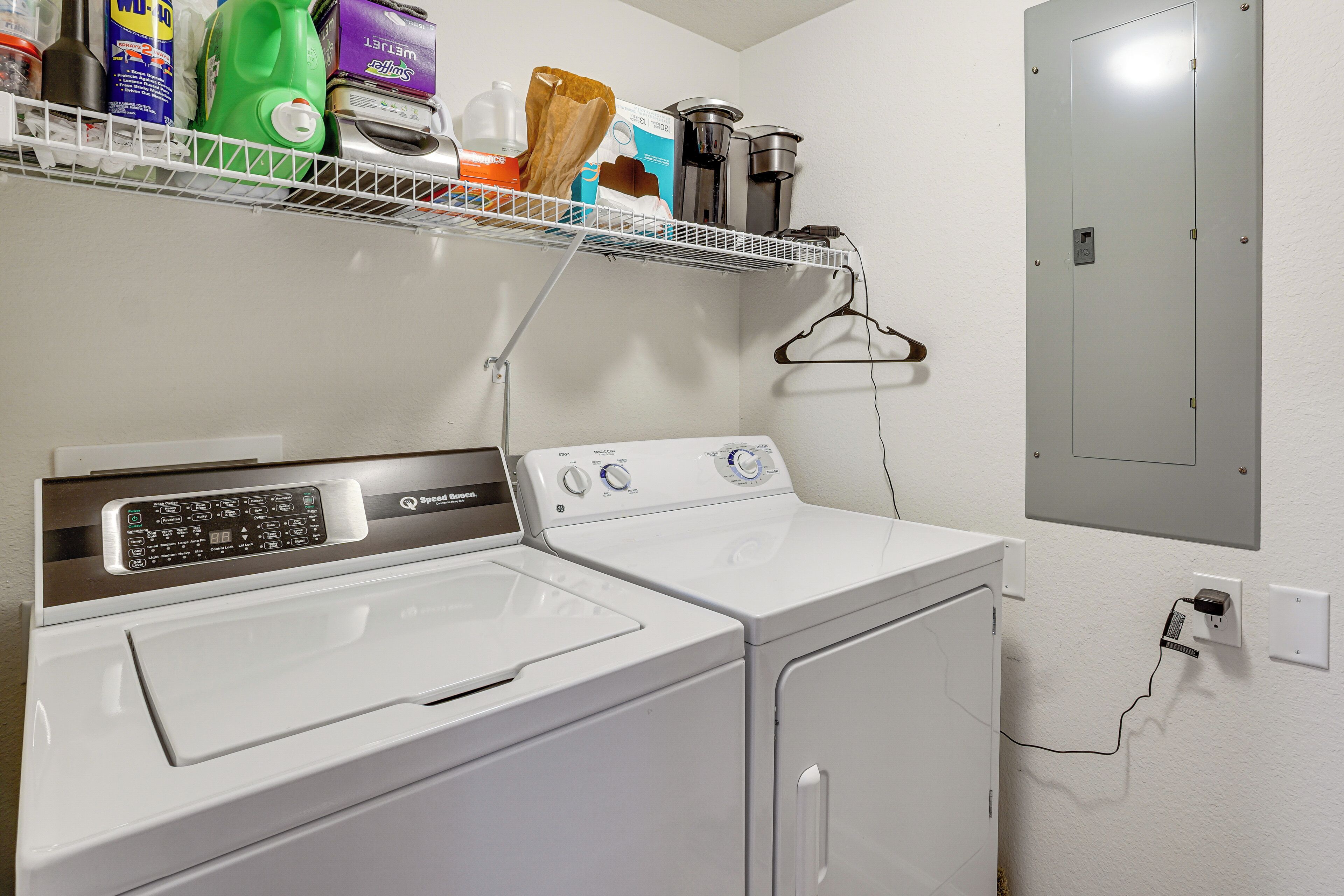 Un espace buanderie comprenant un lave-linge et un sèche-linge à chargement frontal, une étagère avec des produits de nettoyage et un radiateur fixé au mur.