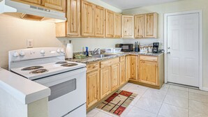 A kitchen with wooden cabinets, a white stove, a microwave, and a sink. - Jmagramo Listing Build Status Details Complete (Ormond Beach)