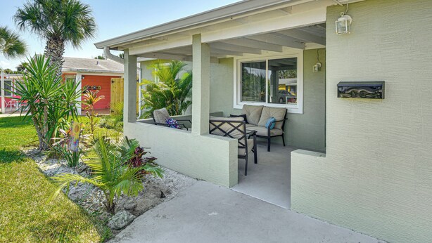 A covered outdoor seating area with chairs and a table, surrounded by tropical plants. - Jmagramo Listing Build Status Details Complete (Ormond Beach)