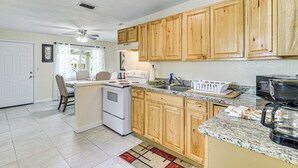 A kitchen with wooden cabinets, a stove, a microwave, and a dining area with chairs and a table. - Jmagramo Listing Build Status Details Complete (Ormond Beach)
