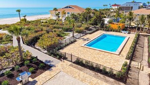 Ein Poolbereich mit freiem Blick auf den Strand, umgeben von üppiger Vegetation und einigen Gebäuden im Hintergrund.