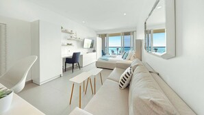 Een moderne woonkamer met een bank, een eethoek en een keuken. Een groot raam biedt uitzicht op zee.