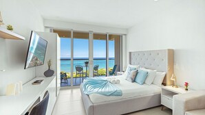 Een moderne slaapkamer met een groot bed, een televisie, een bureau en een balkon met uitzicht op zee.