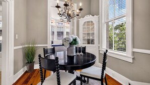 A dining area with a round table, chairs, a chandelier, and a window with blinds. - Southern Charm + Timeless Elegance on Iconic Jones Street By Lucky Savannah (Savannah)
