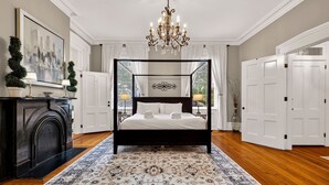 A four-poster bed with white linens, a chandelier, and a patterned rug in a room with wooden flooring and white walls. - Southern Charm + Timeless Elegance on Iconic Jones Street By Lucky Savannah (Savannah)