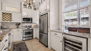 A modern kitchen with white cabinetry, stainless steel appliances, a chandelier, and a view through the window. - Southern Charm + Timeless Elegance on Iconic Jones Street By Lucky Savannah (Savannah)