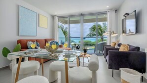Una sala de estar moderna con una mesa de comedor de vidrio, sillas blancas, un sofá y vista al océano.
