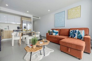A modern living room with a sofa, coffee table, and a dining area with chairs and a table.