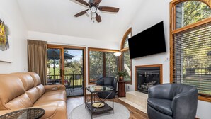 A living room with a leather sofa, a glass coffee table, a black armchair, a fireplace, and a TV mounted on the wall.