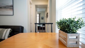 A wooden dining table with a potted plant, a black couch, and a view of a hallway with a dining area in the background.
