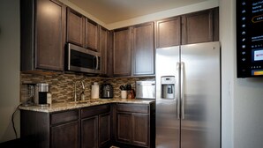 A kitchen with dark wooden cabinets, stainless steel appliances, a coffee maker, and a tiled backsplash.
