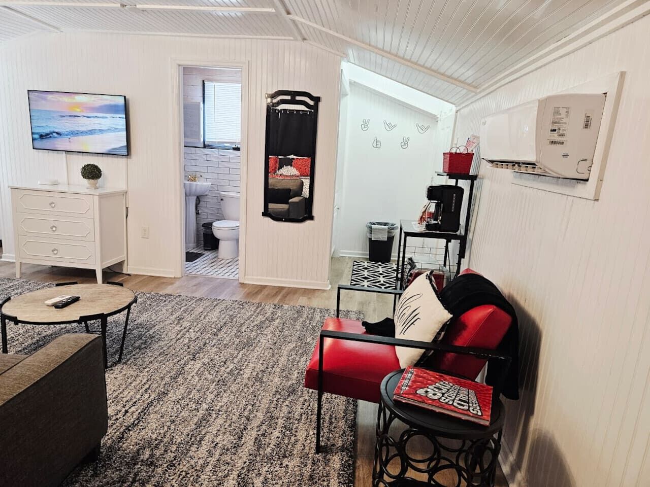 Un salon avec un téléviseur, un fauteuil rouge, une table basse et une vue sur la cuisine.