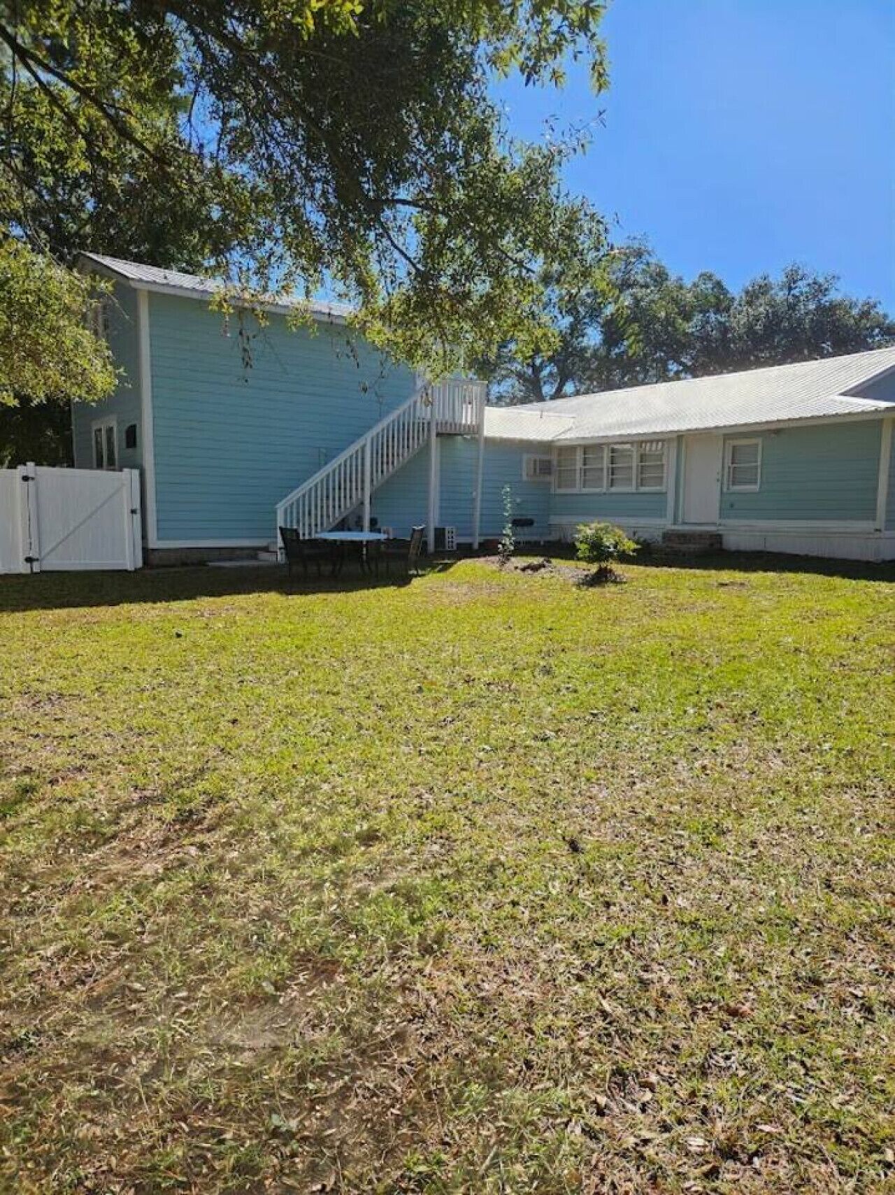 A two-story house with a white staircase, a fenced yard, and a small tree.