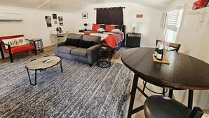 Una sala de estar acogedora con un sofá, una mesa de centro, una mesa de comedor y una cama con colcha roja y negra.