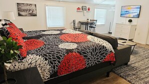 Un dormitorio con una cama grande, un escritorio, una silla y un televisor en la pared.