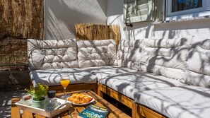 A modern outdoor seating area with a cushioned sofa, a wooden table with a glass, a book, and a plate of food.