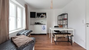 A compact living space with a bed, a dining table with a chair, a kitchenette, and a window with curtains.