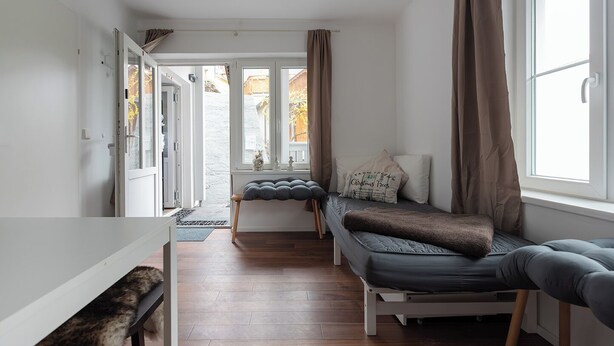 A compact, well-lit room with a bed, a bench, and a window with curtains.