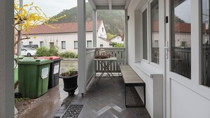 A covered outdoor area with a table and chairs, a trash bin, and a potted plant.
