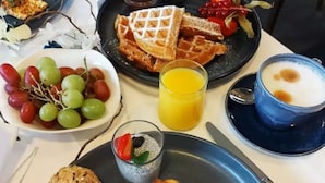 A breakfast setting with waffles, grapes, a glass of orange juice, a bowl of soup, and a dessert.