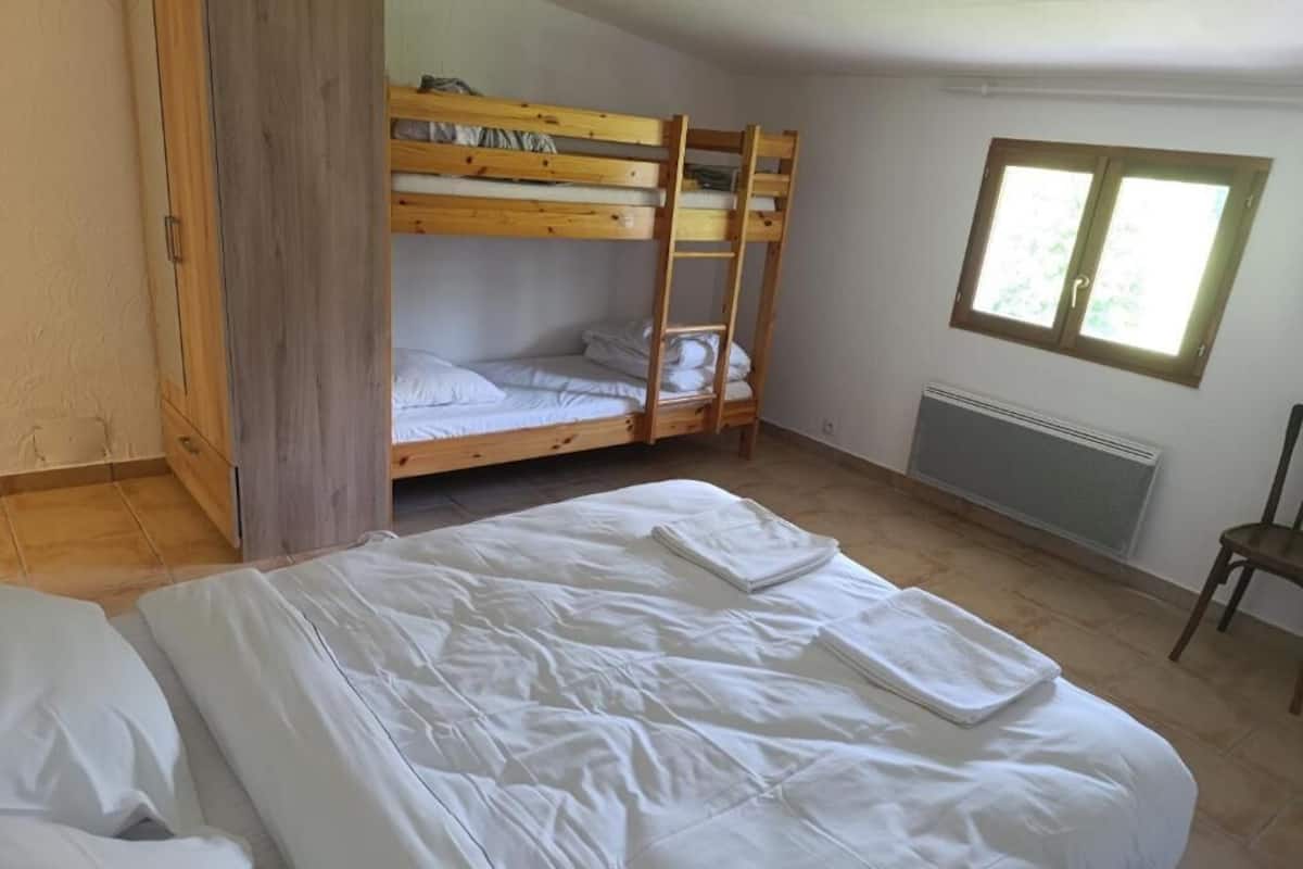 A room with a bunk bed, a single bed, a wooden wardrobe, and a window.