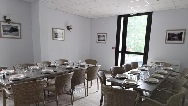 A dining area with long tables set for multiple people, wicker chairs, and framed pictures on the walls. - Le bistrot du berger (Le Vernet)