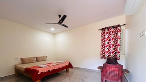 A bedroom with a bed, a ceiling fan, a red patterned curtain, and a red plastic chair. - Whispering Rocks Jungle Resort (Gangavathi)