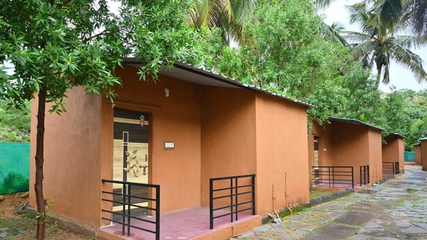 A row of single-story, orange-roofed cottages with black railings, arranged along a stone-paved path. - Whispering Rocks Jungle Resort (Gangavathi)