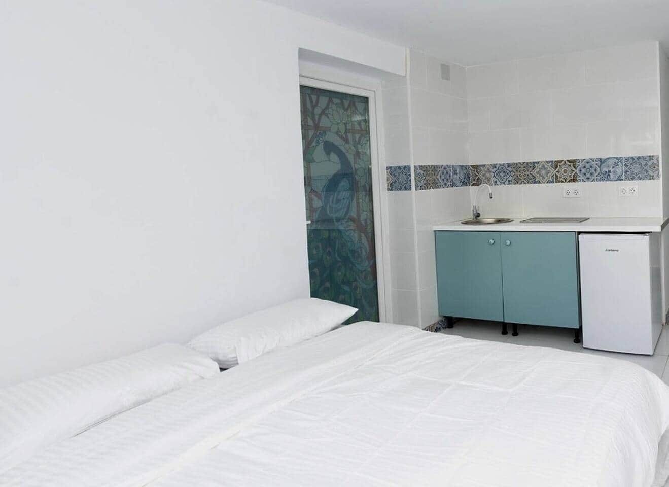 A small, clean room with a bed, a kitchenette, and a door with a decorative panel.