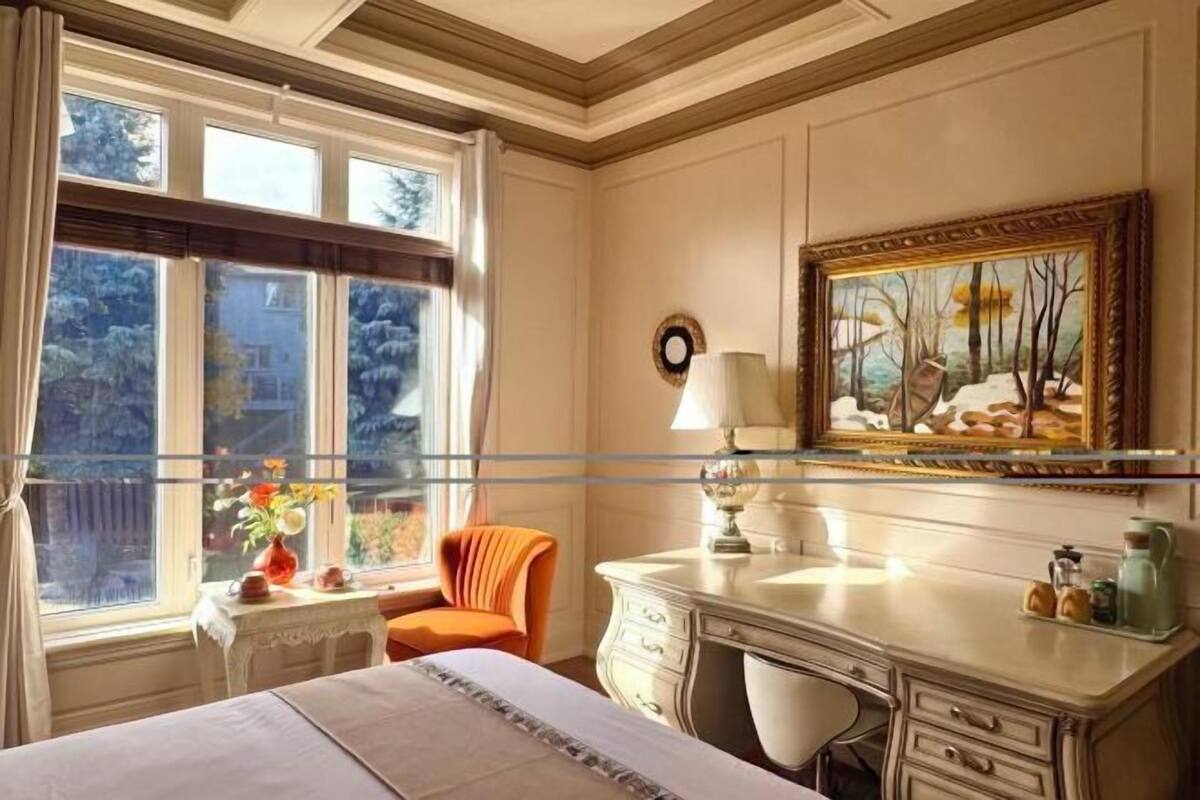 Quarto de hotel com cama, escrivaninha, cadeira, janela com cortinas e um quadro na parede.