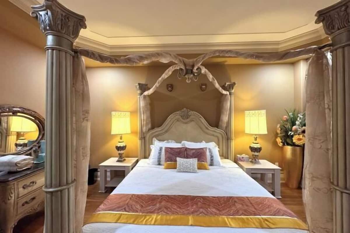 Um quarto luxuoso com uma cama grande, cabeceira decorada e duas mesas de cabeceira com luminárias.