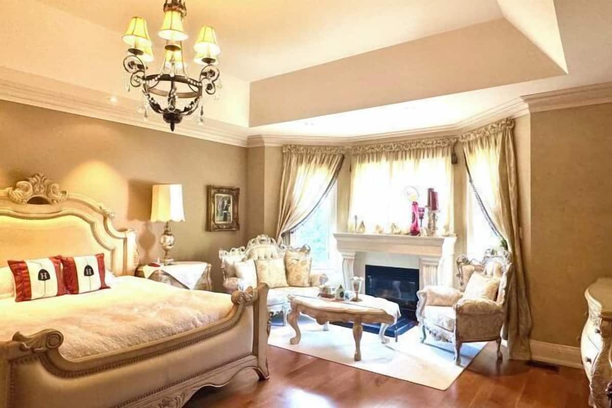 Um quarto espaçoso com uma cama grande, um candelabro, uma lareira e um espaço de estar com um sofá e poltronas.
