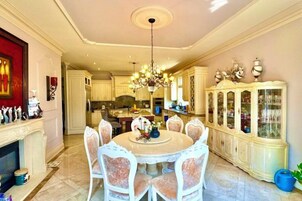 Un comedor amplio con una mesa redonda y sillas, una araña y un mueble grande con puertas de vidrio.