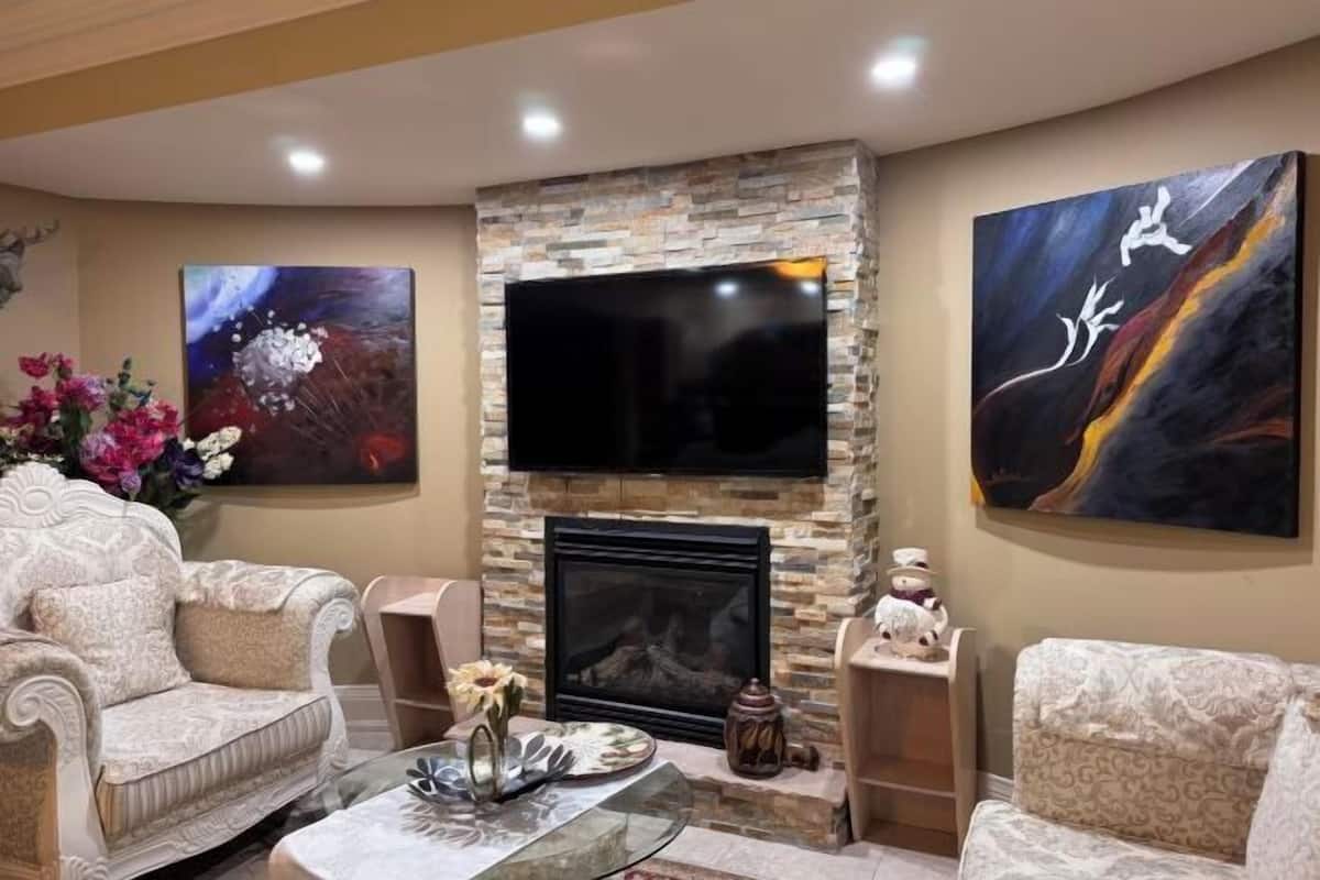 Uma sala de estar com lareira, uma TV de tela plana montada acima, dois sofás e duas mesas laterais com objetos decorativos.