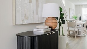 Ein modernes Wohnzimmer mit einem schwarzen Konsolentisch, einem weißen abstrakten Gemälde und einem Essbereich im Hintergrund.