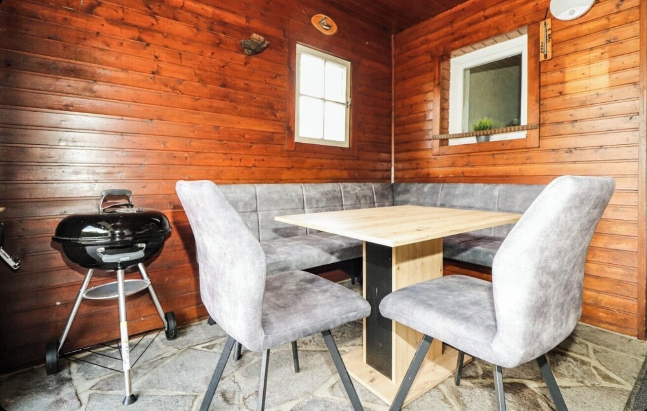 Uma cabana de madeira com área de jantar, incluindo uma mesa e duas cadeiras estofadas cinzas.