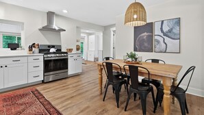 Eine moderne Küche mit weißen Schränken, einem Edelstahlherd und einem Essbereich mit einem Holztisch und schwarzen Stühlen.