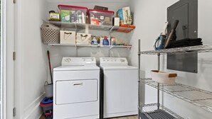 A laundry area with two washers and dryers, shelves with storage bins, and cleaning supplies. - Union Pier home w/Heated pool fire pit screened porch large yard (Union Pier)