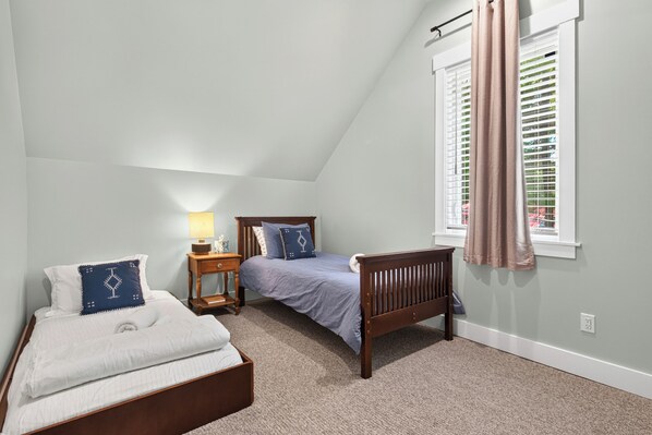 A bedroom with a sloped ceiling, a bed, a bedside table, a lamp, and a window with blinds. - Union Pier home w/Heated pool fire pit screened porch large yard (Union Pier)