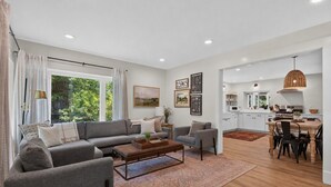 A modern living room with a grey sofa, a coffee table, and a dining area with a wooden table and chairs. - Union Pier home w/Heated pool fire pit screened porch large yard (Union Pier)