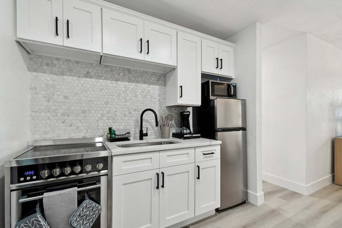 A modern kitchen with white cabinets, a stainless steel oven, a microwave, and a refrigerator.