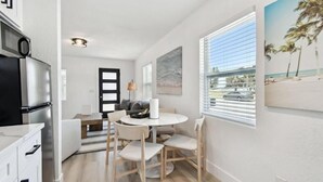 Eine moderne Küche mit Kühlschrank, ein Essbereich mit Tisch und Stühlen und Blick auf den Strand durch große Fenster.