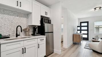 Una cocina moderna con armarios blancos, un refrigerador de acero inoxidable y un microondas.