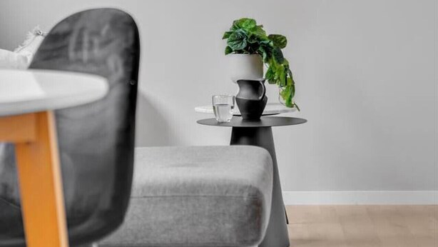 A modern room with a grey sofa, a small table with a potted plant, and a window with a view of the outside.